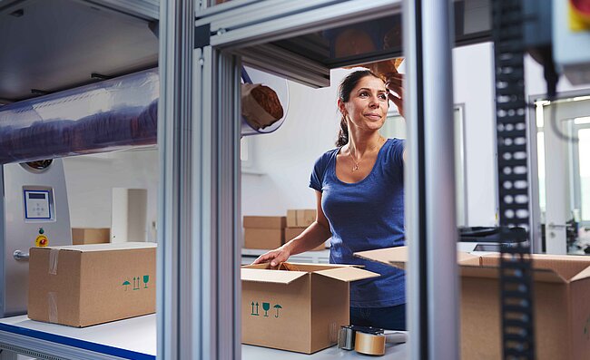 Eine Frau verpackt Produkte im Karton an einer Packstation